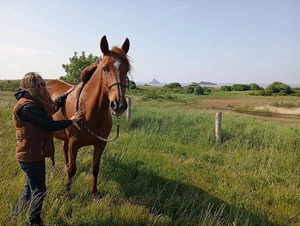 Karine Grueau : garde de chevauxr en Normandie se tient à côté d'un cheval dans un champ